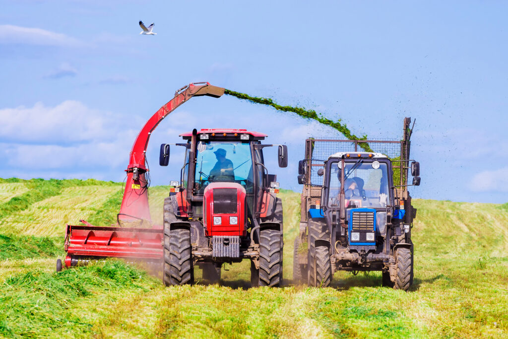 A combination of farm vehicles, one harvesting the farm, and the other catching what the first throws into it. 